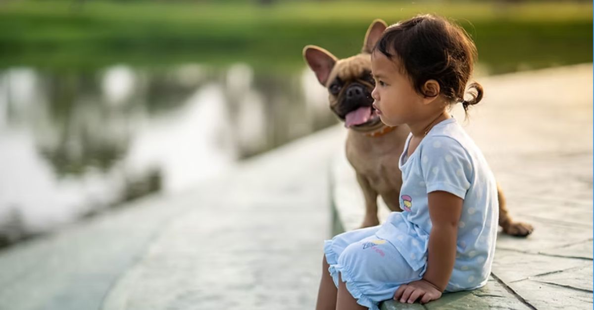 Little girl and her dog sitting by pond