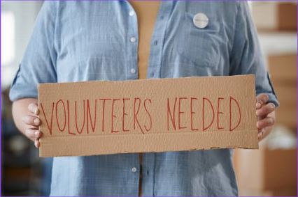 Volunteer holding up 'Volunteers Needed' sign.